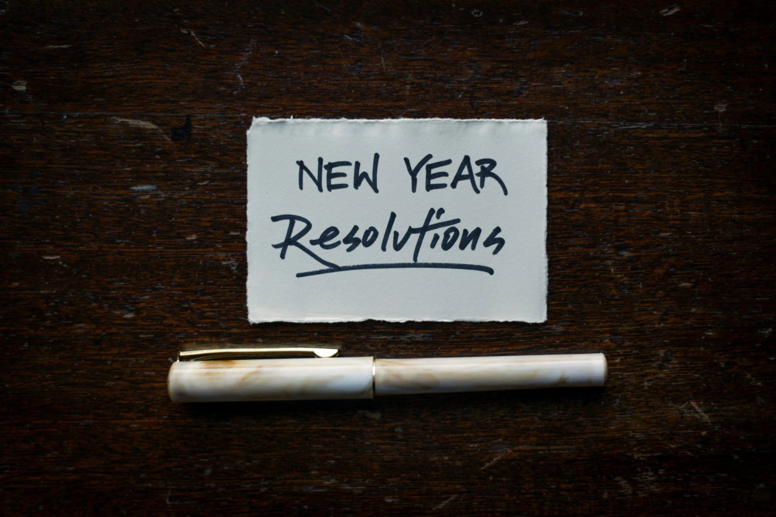 Handwritten New Year Resolutions note beside a pen on a dark wooden table