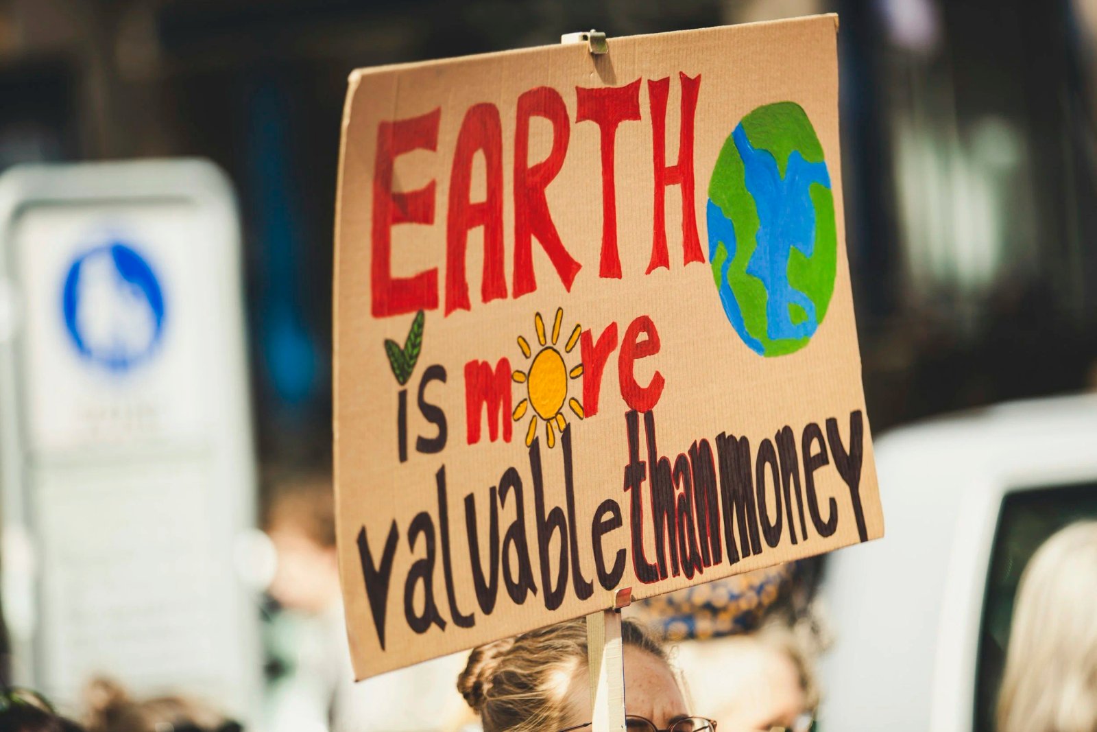 Protest sign painted with a globe and a sun reading Earth is more valuable than money